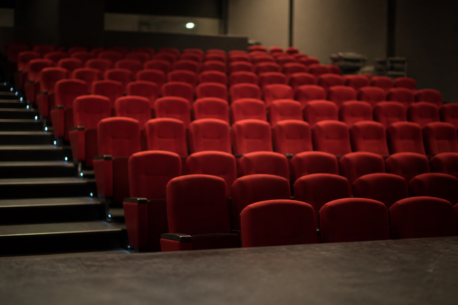 Rang&eacute;es de fauteuils rouges vides dans une salle de spectacle, vues depuis le bord du plateau.